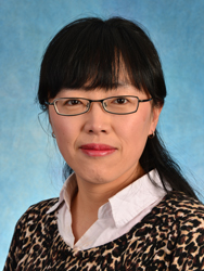 Portrait of Xue Bai. Xue is an Asian woman with straight black hair tied back in a ponytail. She is wearing a white collared shirt, leopard-print sweater, and black-rimmed glasses.